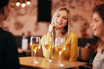 Female friends drinking wine and chatting while sitting in the bar.