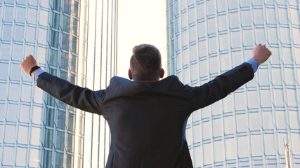 Successful businessman in suit, feels free, skyscraper background. Concept: success, career growth, victory, freedom.