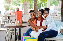 Three Casual African American Girls With Colored Shopping Bags Walking Outdoor. Stylish Black Womans Shopping.
