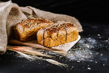 sweet and tasty bread and wheat on black wooden background