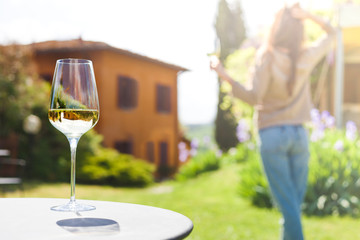 Wall Mural - glass of chilled white wine on table over young woman and Tuscany backgound