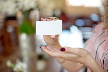 Female hand with neat manicure holding white empty blank business card on beautiful blurred background with bokeh.