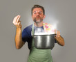 © TheVisualsYouNeed - young attractive happy and proud home cook man cooking soup holding kitchen pot smelling the meal aroma gesturing delighted and satisfied
