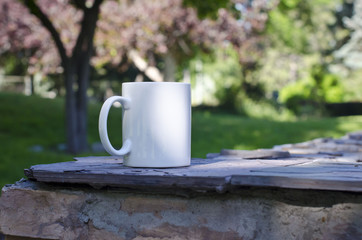 Wall Mural - A blank white coffee mug on the ledge of a park under the pink trees. 