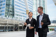 © shutterdemon - Asian business woman holding document file and plastic mug on hand talk about business future with  Caucasian businessman. they are walk together in the city.