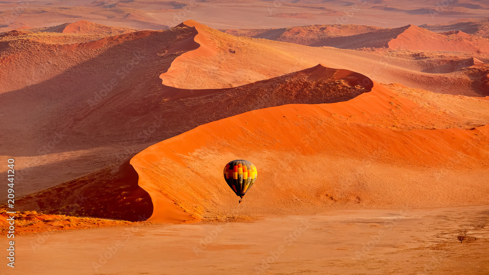 Hot air balloon in flight against orange sand dunes in Sossusvlei Namibia - obrazy, fototapety, plakaty 