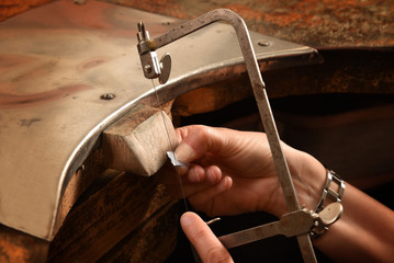 Wall Mural - hands of a female goldsmith work on a piece of silver with a metal saw on the workbench, close up