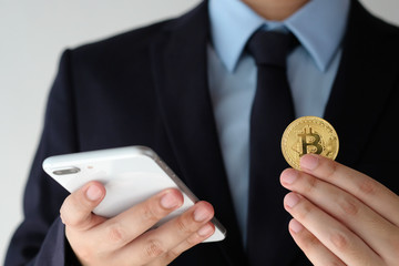 Businessman hand holding bitcoin and using smartphone over white background, blockchain and cryptocurrency concept background