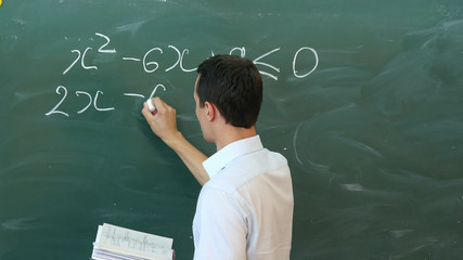Young teacher writing on a blackboard math formula.