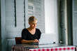 © Danon - A young and attractive blond woman with blue eyes works on her laptop in a cafe during the day.