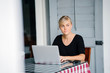 © Danon - A young and attractive blond woman with blue eyes works on her laptop in a cafe during the day.