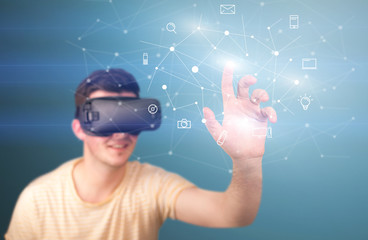 Young impressed man wearing virtual reality goggles with mixed media icons around his finger