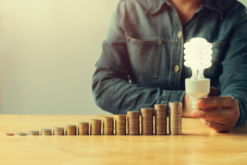 Wall Mural - businessman hand holding led light and money stack on table in office. concept saving money with energy