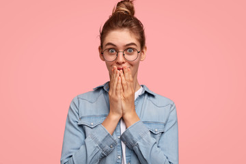 Wall Mural - Indoor shot of pretty pleased female tries to stop giggling, looks joyfully at camera, gossips with friend, discuss colleagues and their personal life, wonders some news, has dark hair tied in bun