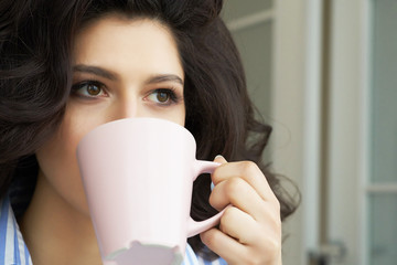 Young girl drinks coffee from a cup slooking into the distance.