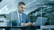 © Gorodenkoff - Confident Handsome Businessman Works on a Laptop at His Desk. Stylish Man in Modern Glass Office.