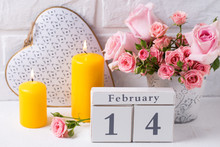  Pink Roses Flowers, Calendar, Decorative Heart  And  Yellow  Candles Against  White Brick Wall.
