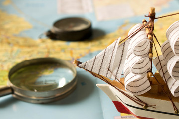 Model sailboat, compass and magnifying glass on map background. Travel concept