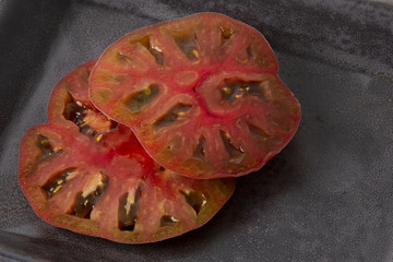 Two large pieces of a black tomato on a plate of gray marble.