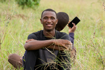 two young men leaning against each other and sitting on the grass in the park