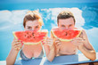 young beautiful couple in pool eating watermelon at sunset