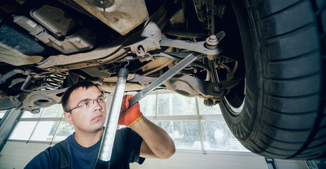 Wall Mural - Car mechanic examining car suspension of lifted automobile at repair service station