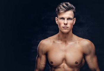 Close-up portrait of a sexy shirtless young man model with a muscular body and stylish haircut posing at a studio. Isolated on dark background.