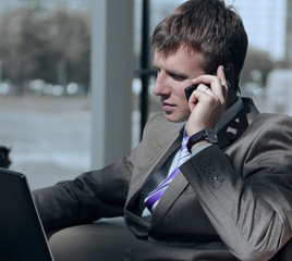 Attractive european guy talking on phone while using laptop.