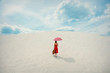© Masson - Young woman in red dress with umbrella and suitcase on the beach. Travel concept image on sand