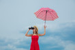 © Masson - Young woman in red dress with umbrella and binoculars on the beach. Travel concept image
