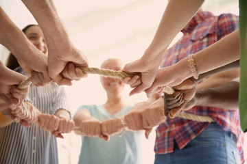 Wall Mural - People holding rope together on light background, closeup of hands. Unity concept