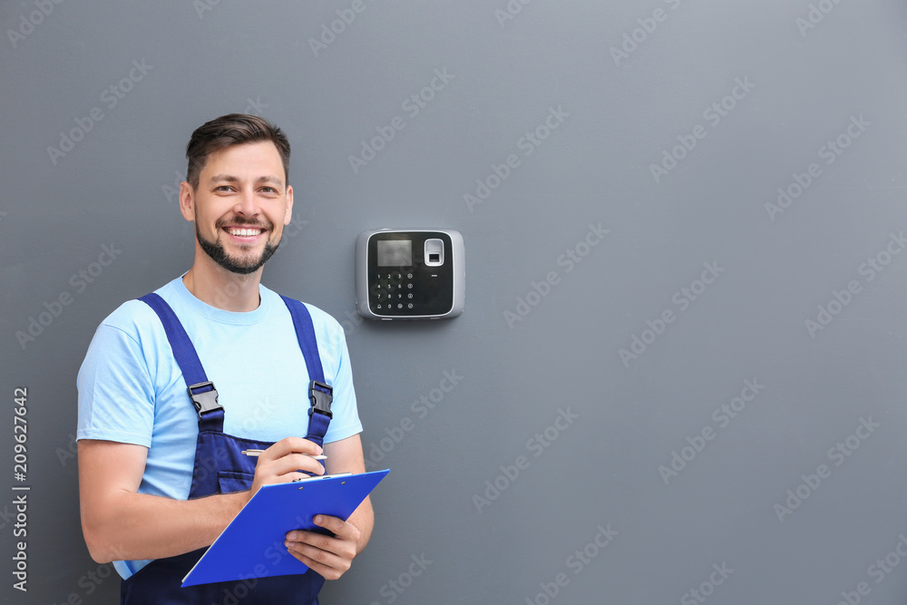 Male technician with clipboard near installed alarm system indoors - obrazy, fototapety, plakaty 