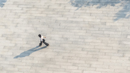 Wall Mural - people walk on across the pedestrian concrete landscape with black silhouette shadow on ground (top aerial view)