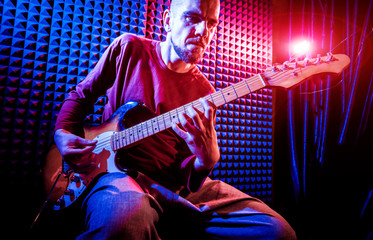 Young man playing on the guitar in sound recording studio.