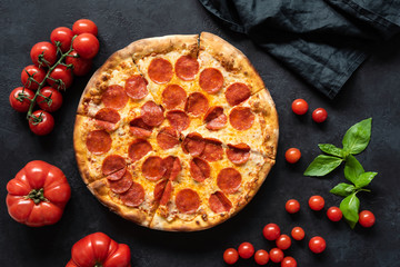 Hot pepperoni pizza on black stone background. Sliced tasty pizza with salami, cheese and tomatoes on dark table, top view