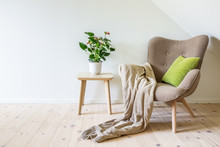 Beige Armchair With A Green Pillow, Blanket And A Wooden Table With A Potted Plant (Anthurium). Empty White Wall In Simple Living Room Interior. Copy Space