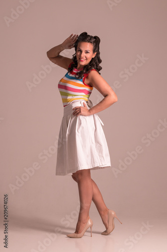 Poster Pretty woman in skirt with hairdo poses in grey studio, pin up style, full body