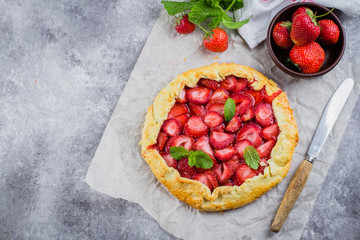 Wall Mural - Galette with strawberry on the gray concrete stone background. Vegetarian healthy berry tart decorated with fresh sliced strawberries and mint. Delicious summer food dessert. Top view, copy space