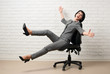 © soleg - the business woman having fun, falls from chair, dressed in a gray suit poses in front of a white wall