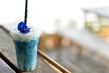 Iced Blue Pea Milk Or Iced Butterfly Pea Latte With Milk On The Wooden Table And Blurred Nature Background. Copy Space