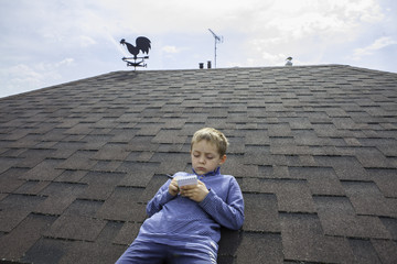 Boy is on a roof and write a book at suumme in backgroun blue sky.