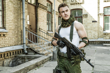 Wall Mural - Young male military soldier with a rifle near the old building