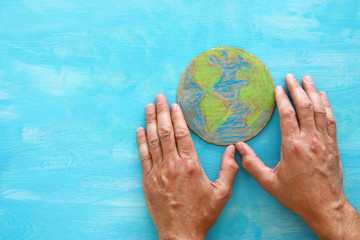 top view image of man hands holding earth globe over blue wooden background.