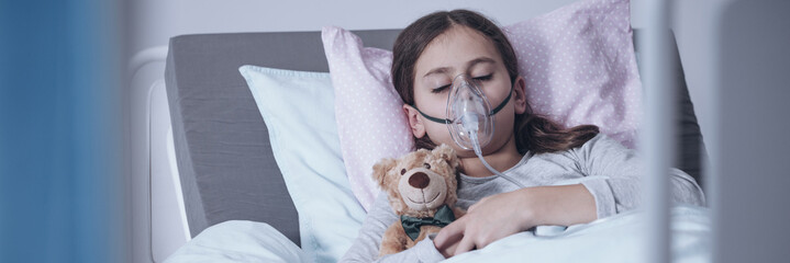 sick young girl in a hospital bed sleeping with an oxygen mask and a toy, getting treatment for cyst