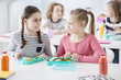 © Photographee.eu - Front view of two girls sitting by a school desk with opened lunch boxes with healthy vegetables and sandwiches. Bottles of orange and tomato juice on a desk. Other children in blurred background