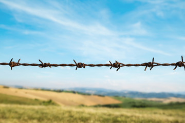 Fence with barbed wire, fields and blue sky on background