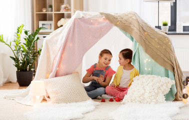 Sticker - childhood and hygge concept - happy little girls playing tea party with toy crockery in kids tent at home