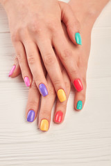 Wall Mural - Well-groomed hands with summer manicure. Young woman nails covered with different colors polish on white wooden background. Perfect summer manicure.