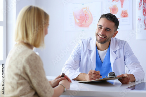 Fotomural Handsome doctor is talking with young female patient and making notes while sitt