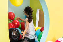 Rear View Of A Cute Girl Wearing White T-shirt While Playing With Colorful Balloons During Playtime At The Kindergarten